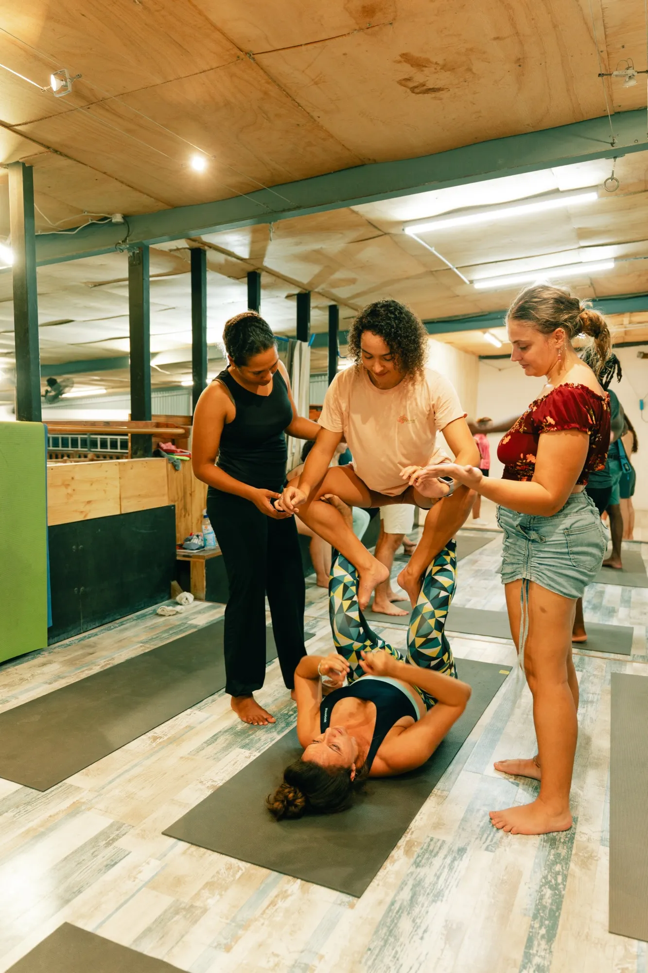 Cours d’acroyoga au studio : une élève portée sur les pieds de sa partenaire, deux personnes assurent la parade