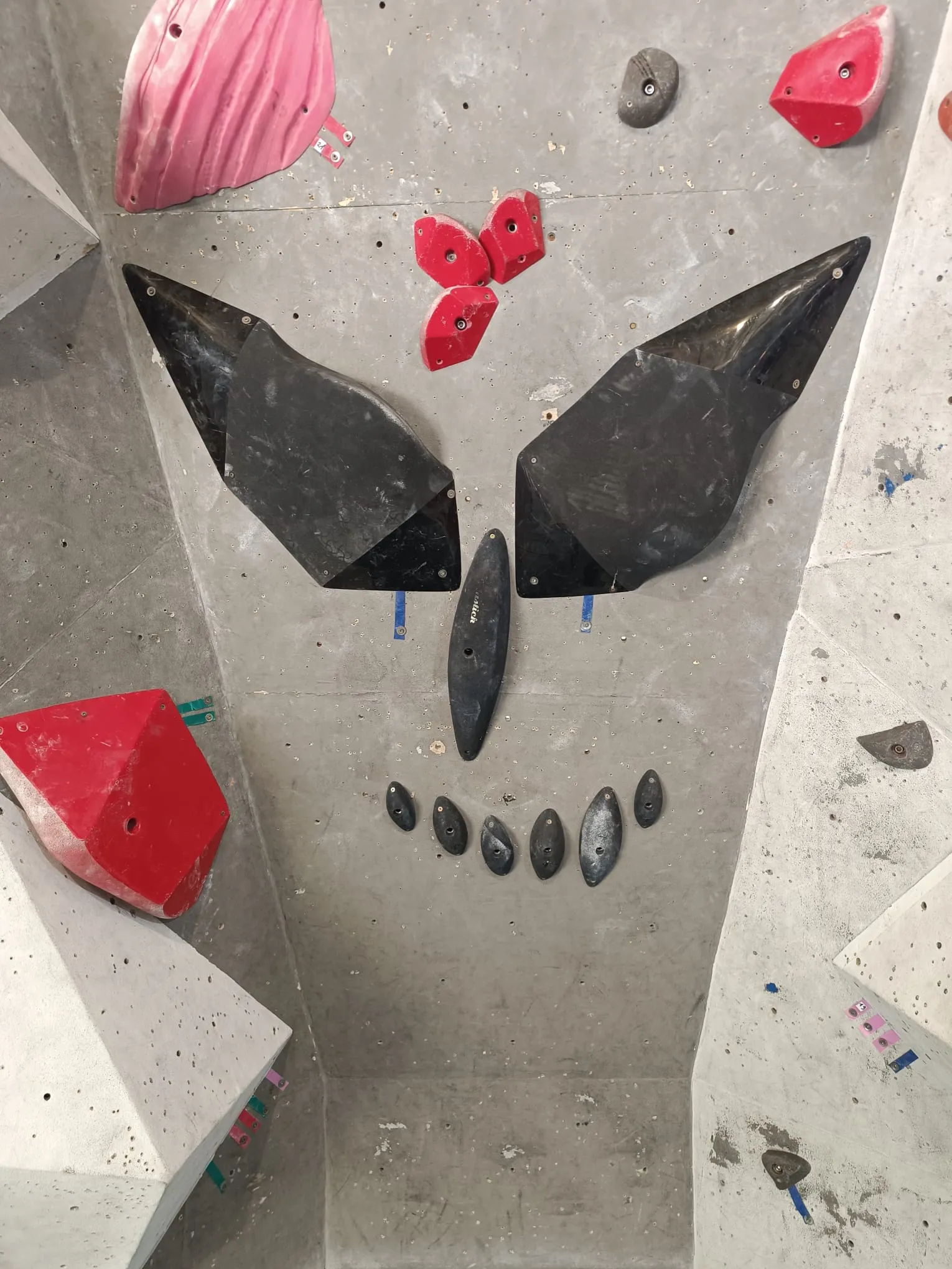 Tête de mort dessinée sur le mur d’escalade avec des prises noires : deux grands volumes pour les yeux, une prise pour le nez et une rangée de petites prises pour les dents
